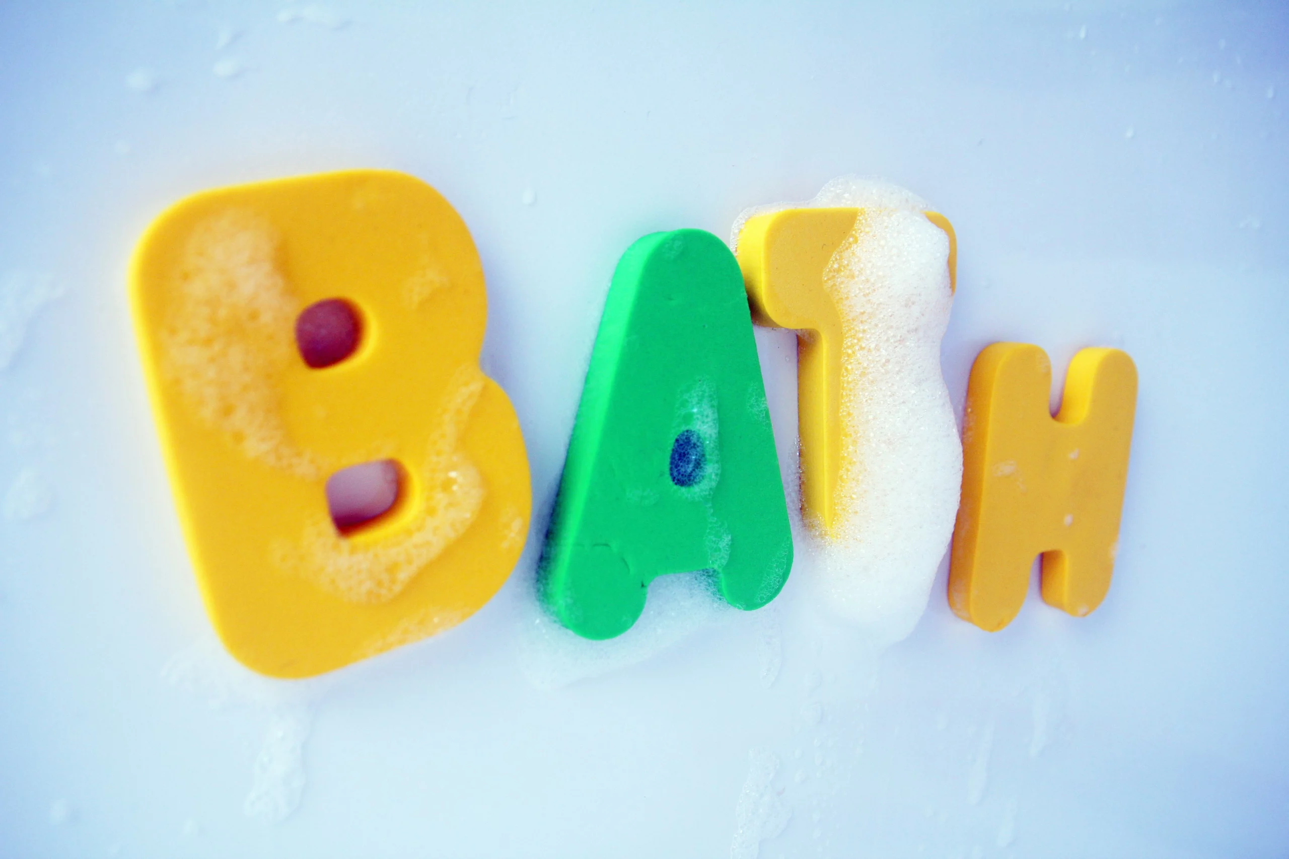 Bain écrit en anglais avec les couleurs : jaune et vertes et de la mousse sur fond bleu